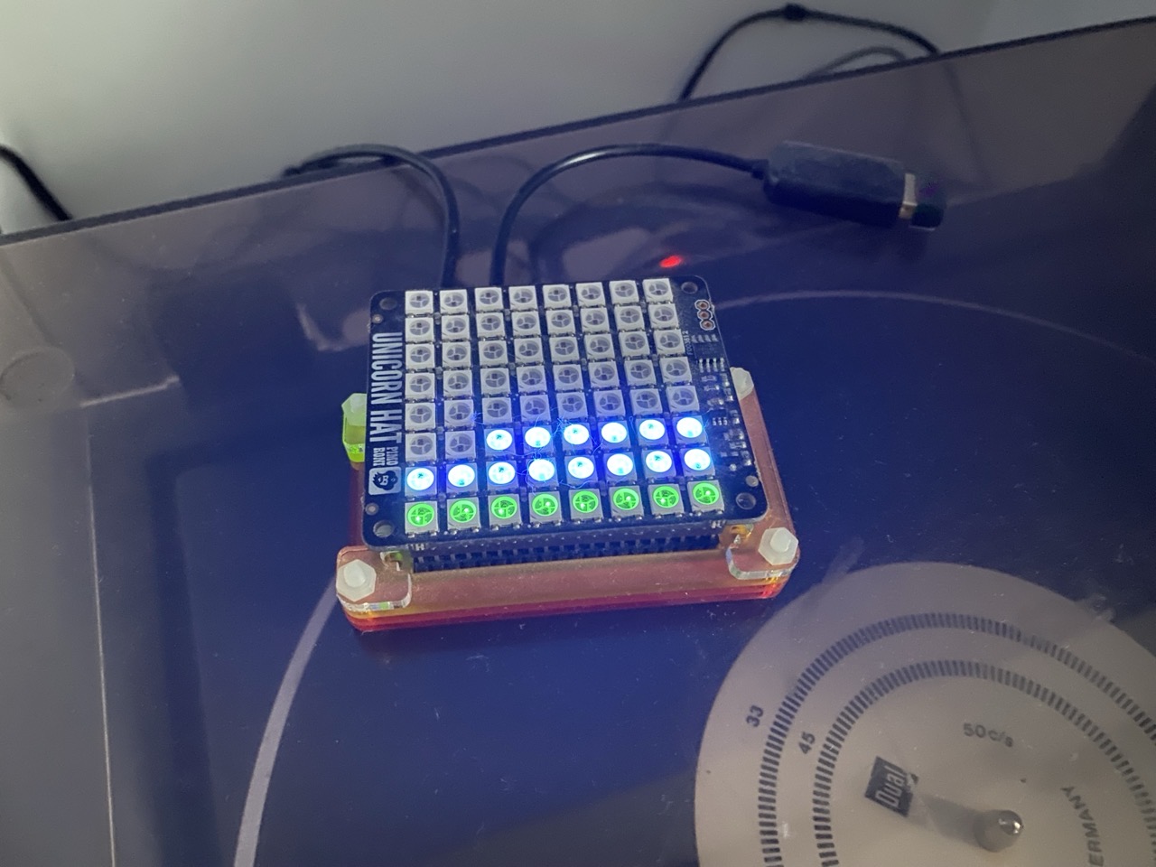 A raspberry pi zero with a grid of lights on it. The lights are blue and green in a pattern that suggests a graph over time. Two people are in game.