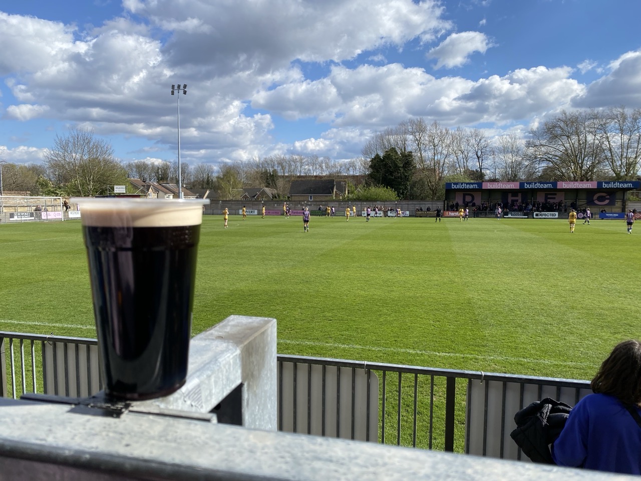 A pint sitting on a fence, with Dulwich Hamlet FC playing in the background