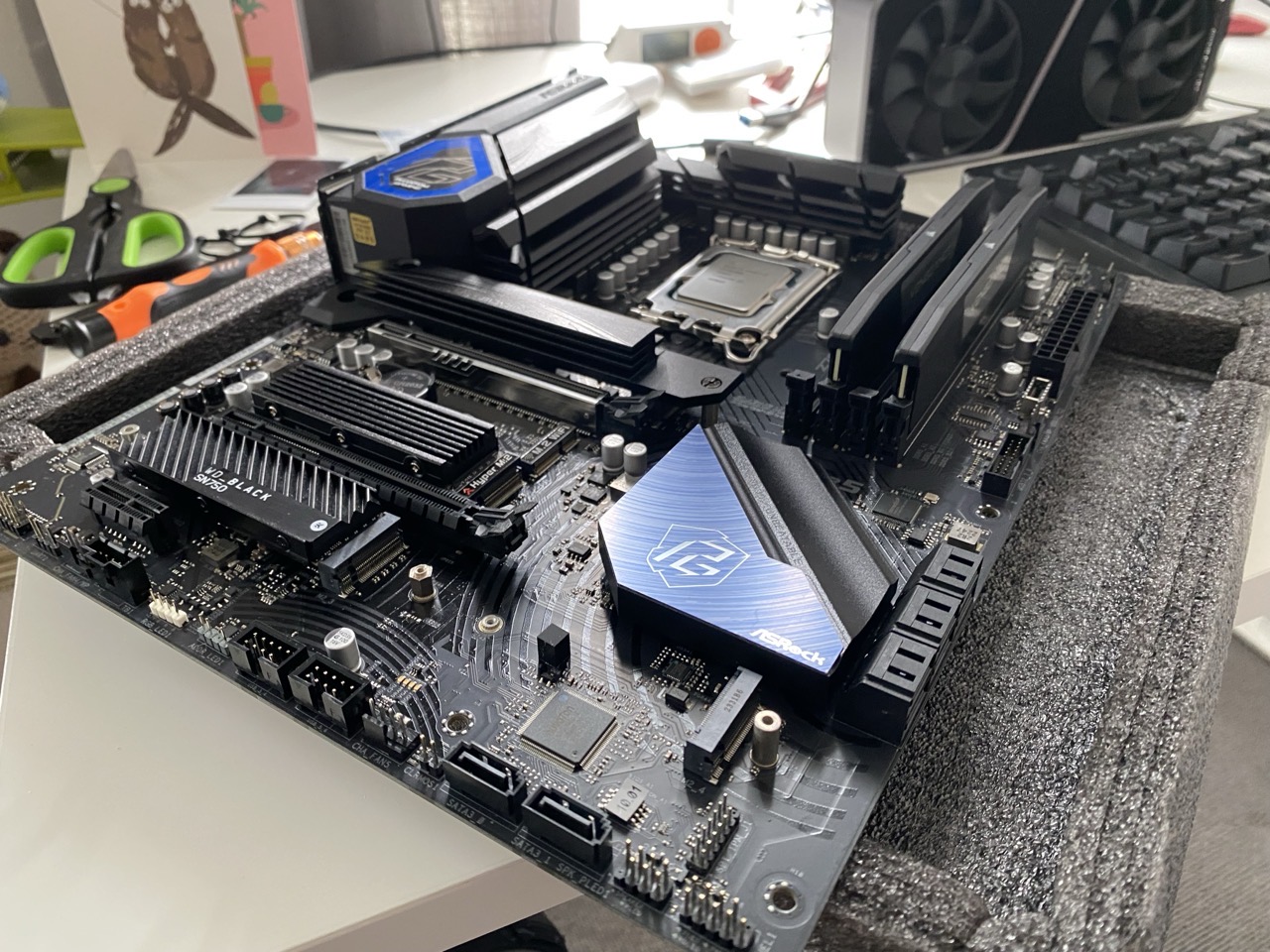 A computer motherboard sitting on a white desk. The memory banks and CPU have been installed.