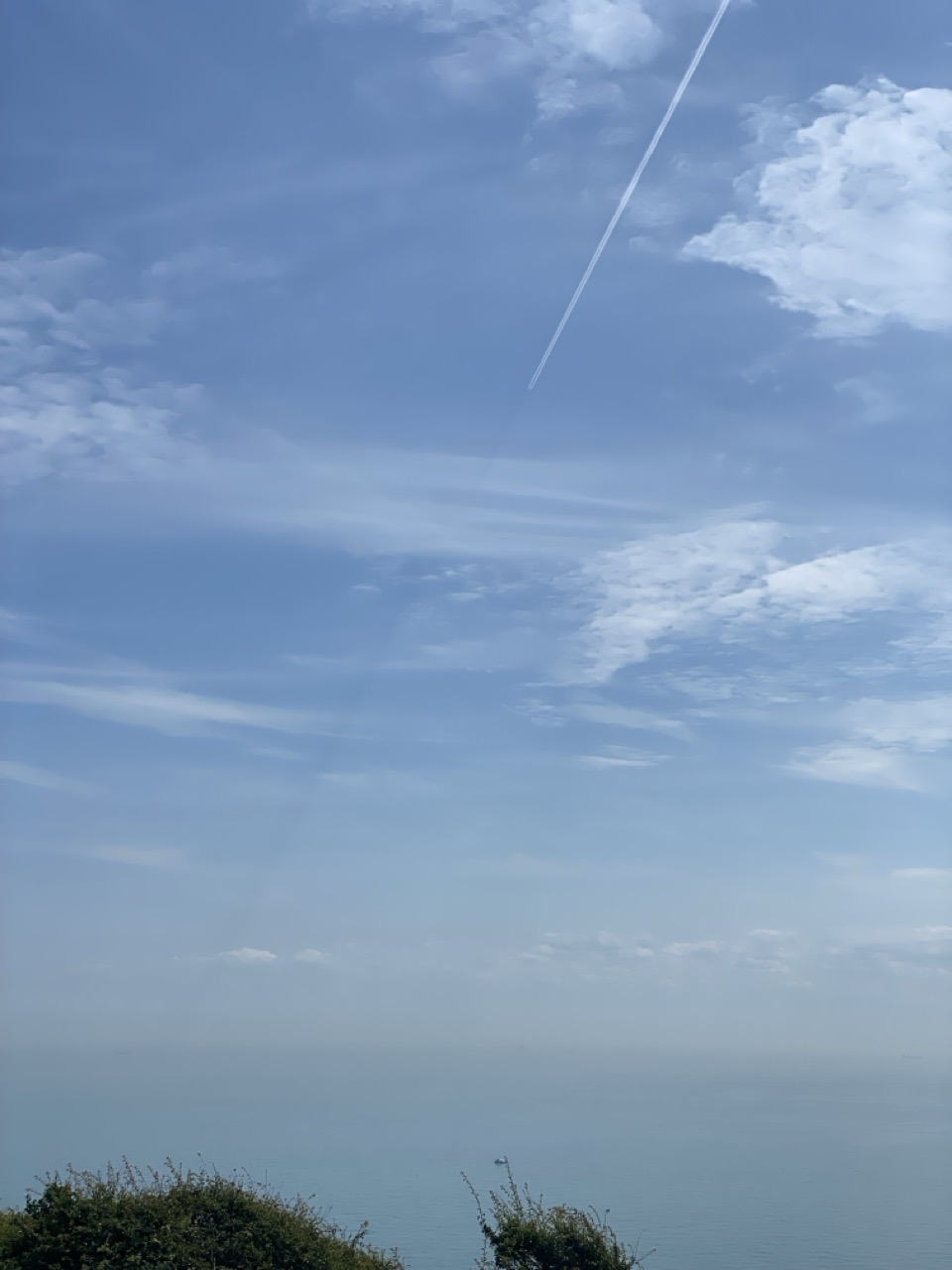A blue sky over the sea with a jet contrail and a shadow extending from it towards the horizon.