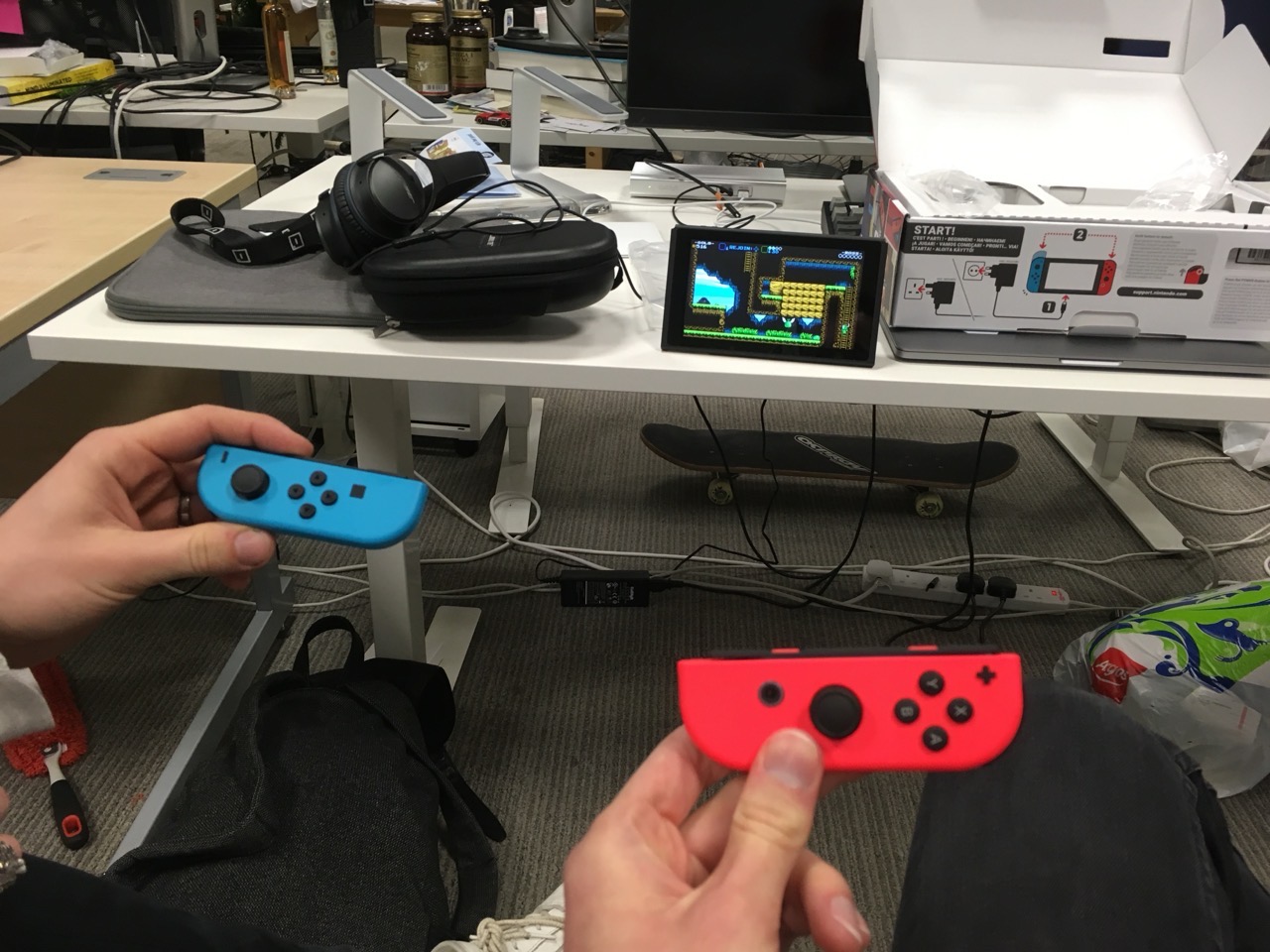 The switch on a desk. Two people are holding joy cons in the foreground