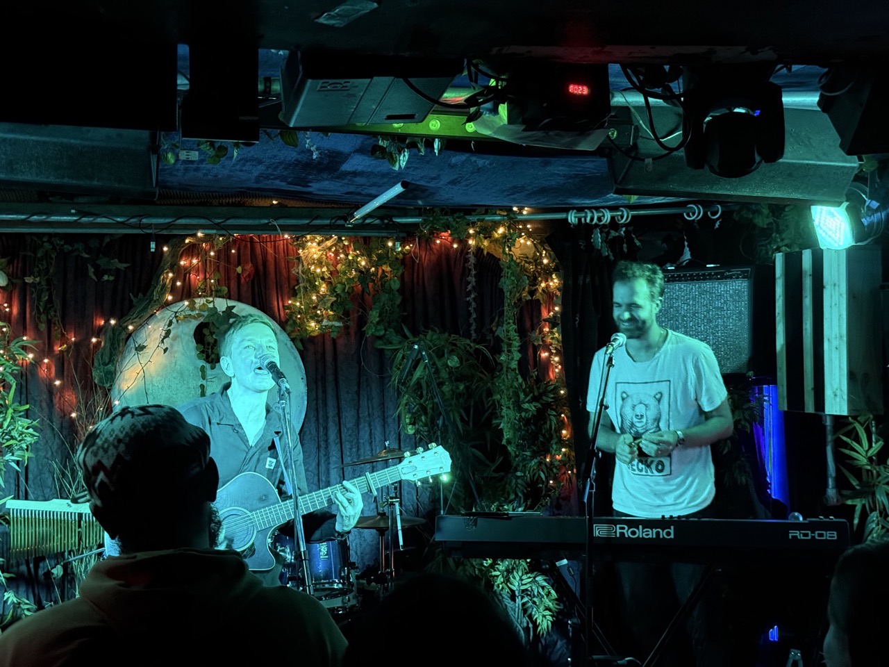 Gecko and Chris on stage, Gecko is to the left on guitar and Chris is playing keys and shaking an egg thing